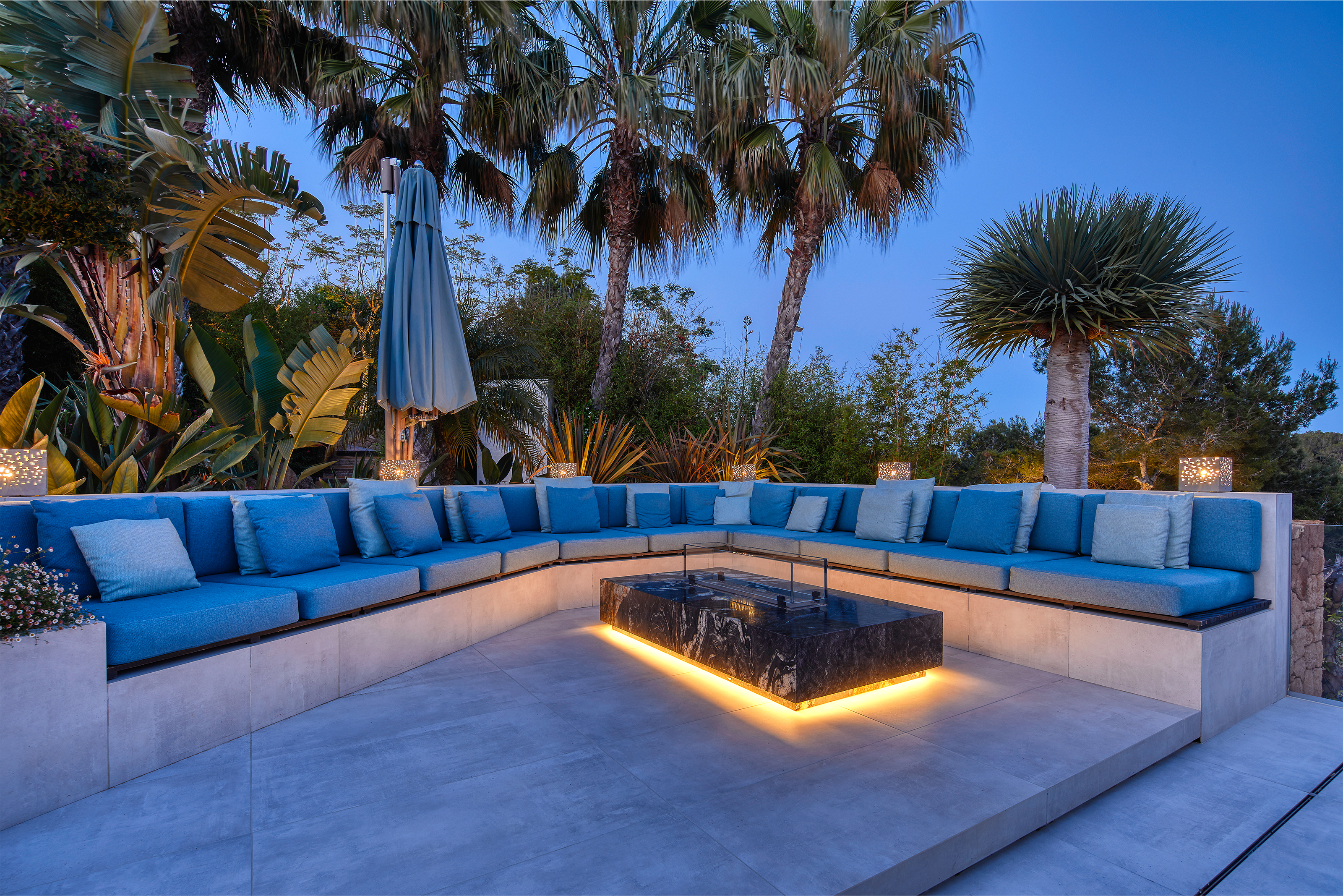 Terrasse luxueuse avec carreaux extérieurs modernes, salon bleu et palmiers au crépuscule.