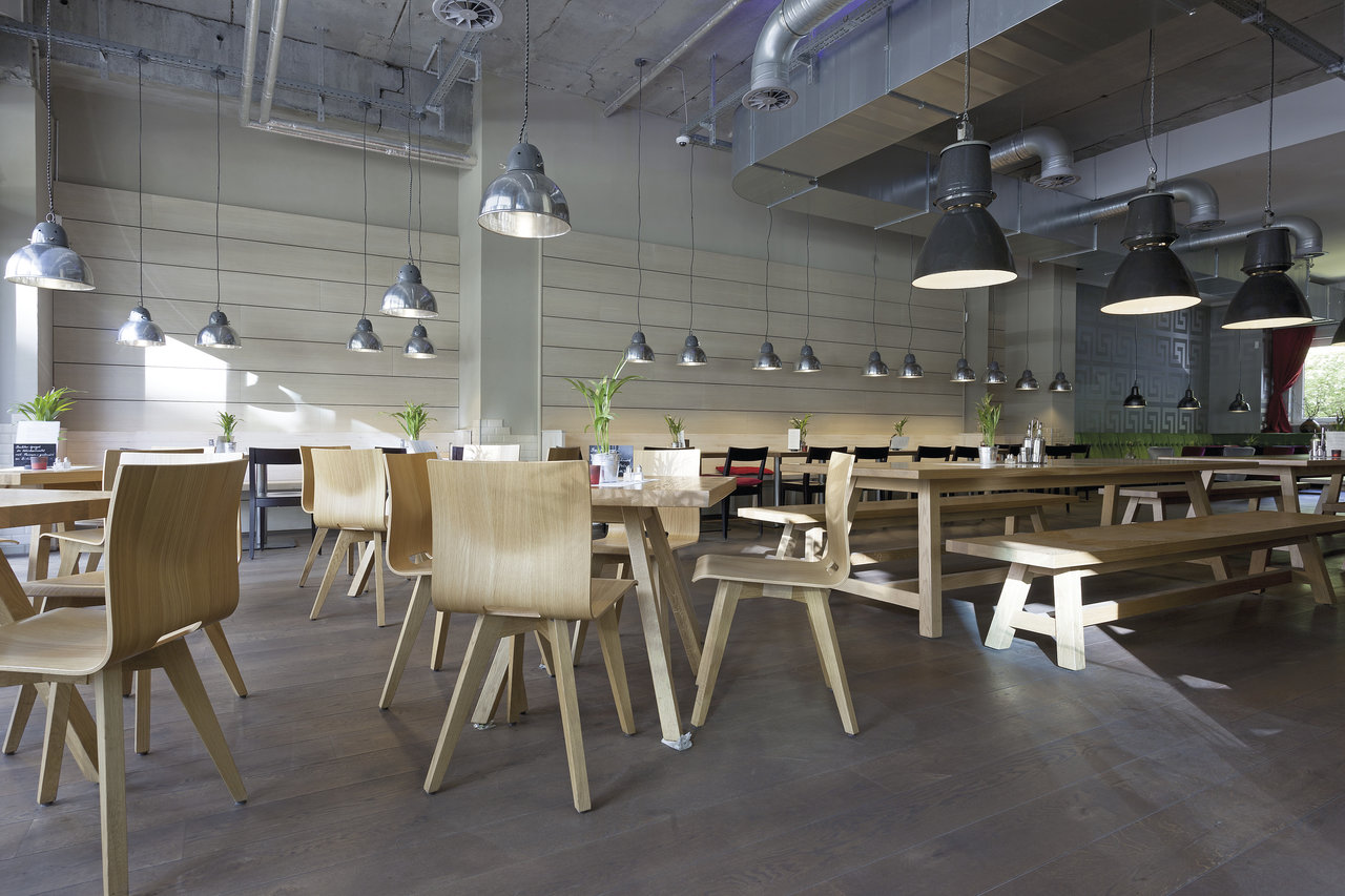 Intérieur spacieux et lumineux avec tables en bois et sol carrelé moderne aspect béton.