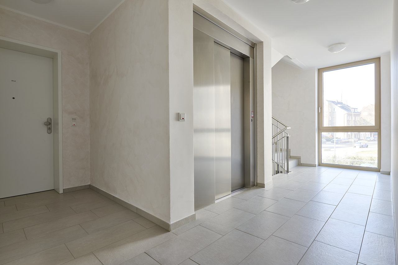 Couloir lumineux avec des carreaux de sol modernes gris clair et un ascenseur.