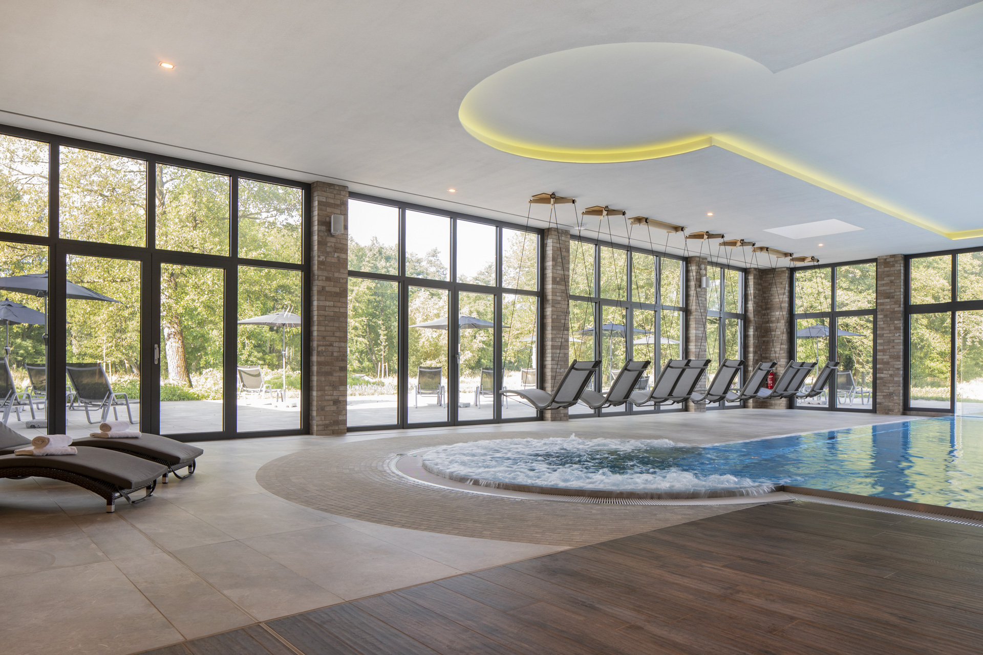 Luxueux espace piscine intérieur avec carrelage élégant Porcelaingres et Schöner Wohnen, jacuzzi et vue sur la verdure.