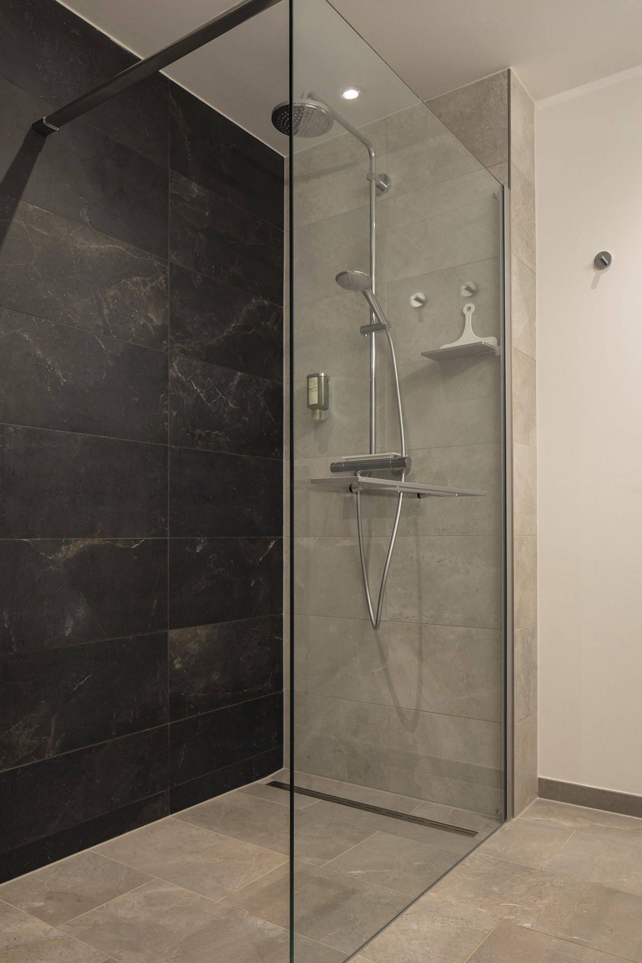 Carrelage de qualité dans douche moderne : murs foncés, sol et murs gris clair.