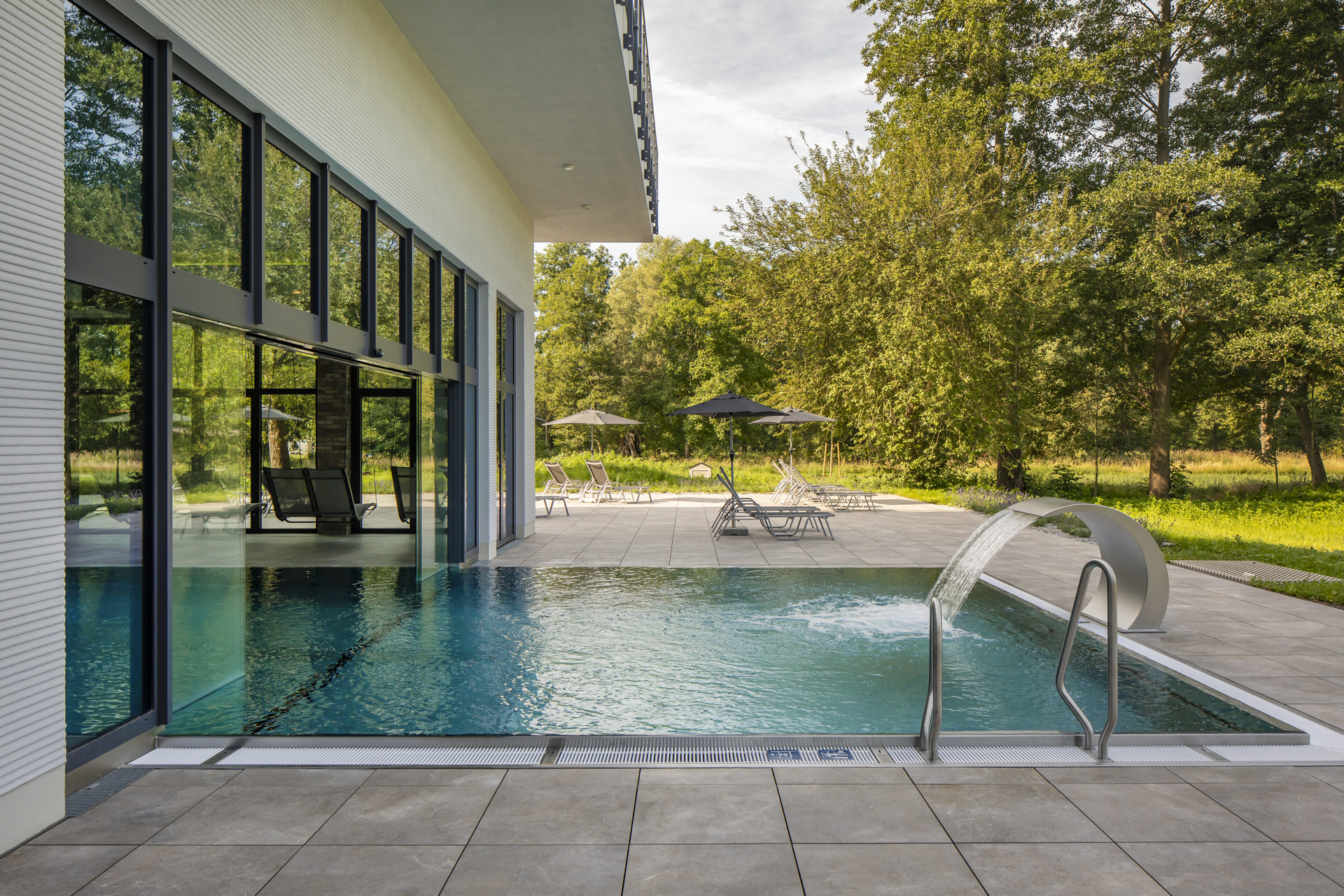 Carreaux d'extérieur de haute qualité pour une piscine élégante avec cascade et façade en verre moderne.
