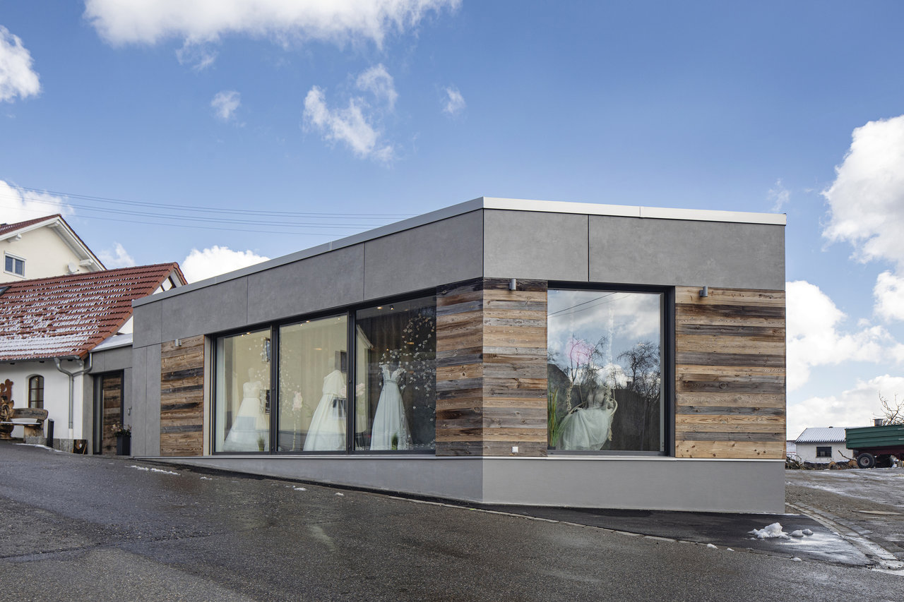 Façade moderne grise et revêtement bois, avec vitrines de robes de mariée.