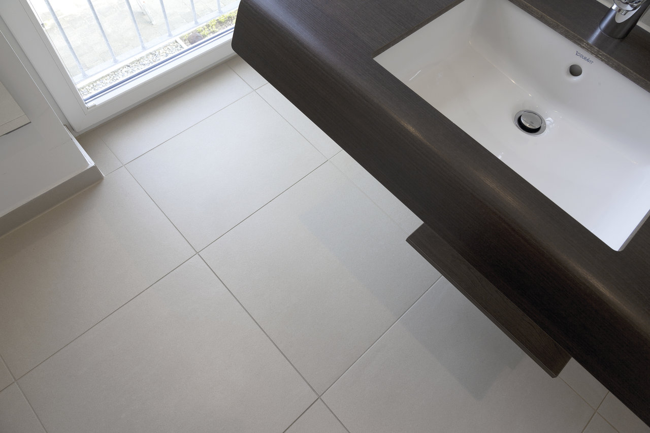 Carreaux de sol clairs et modernes dans la salle de bain à côté d'une vasque foncée.