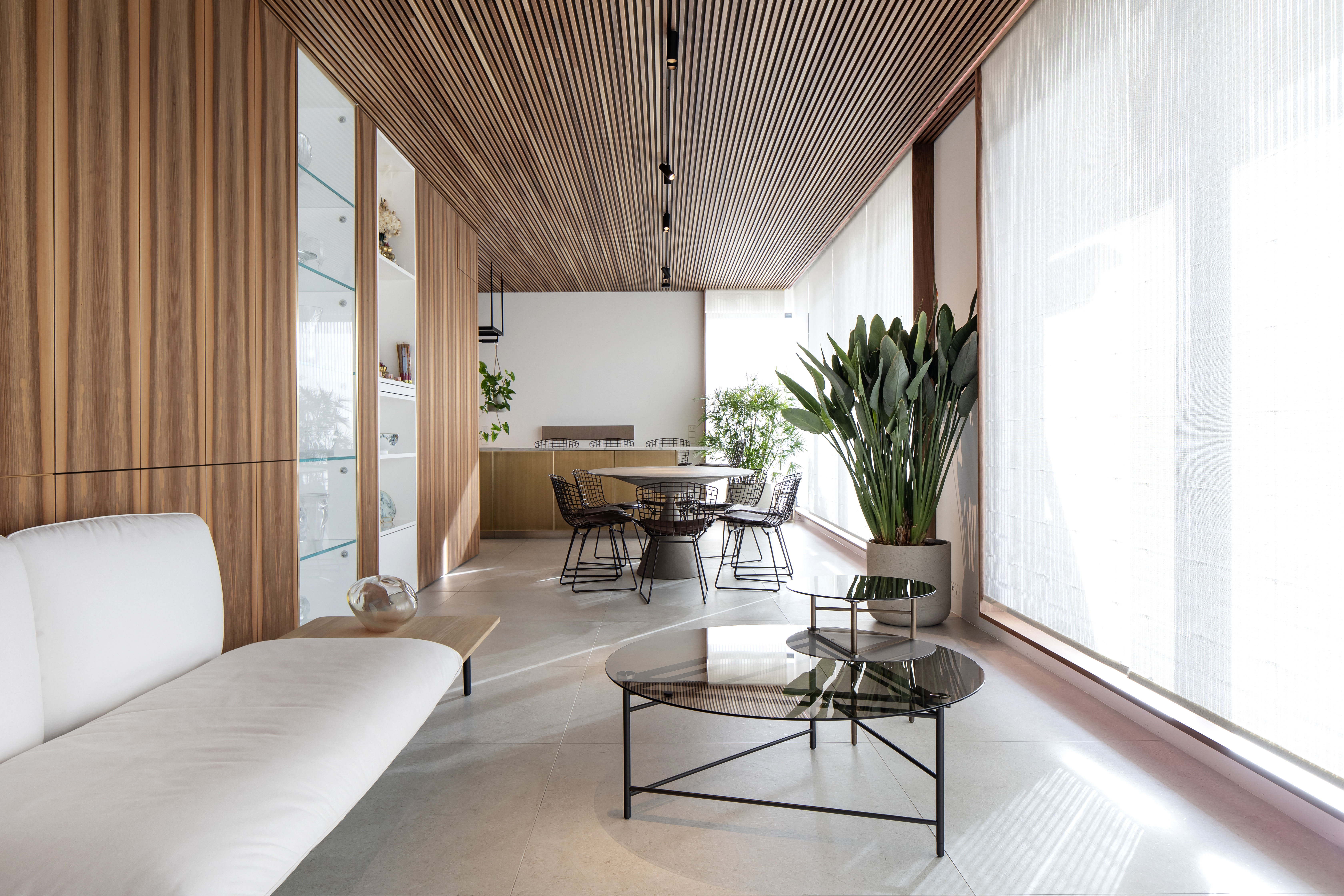 Salon lumineux et moderne avec carrelage grand format aspect béton, plafond bois et plantes.