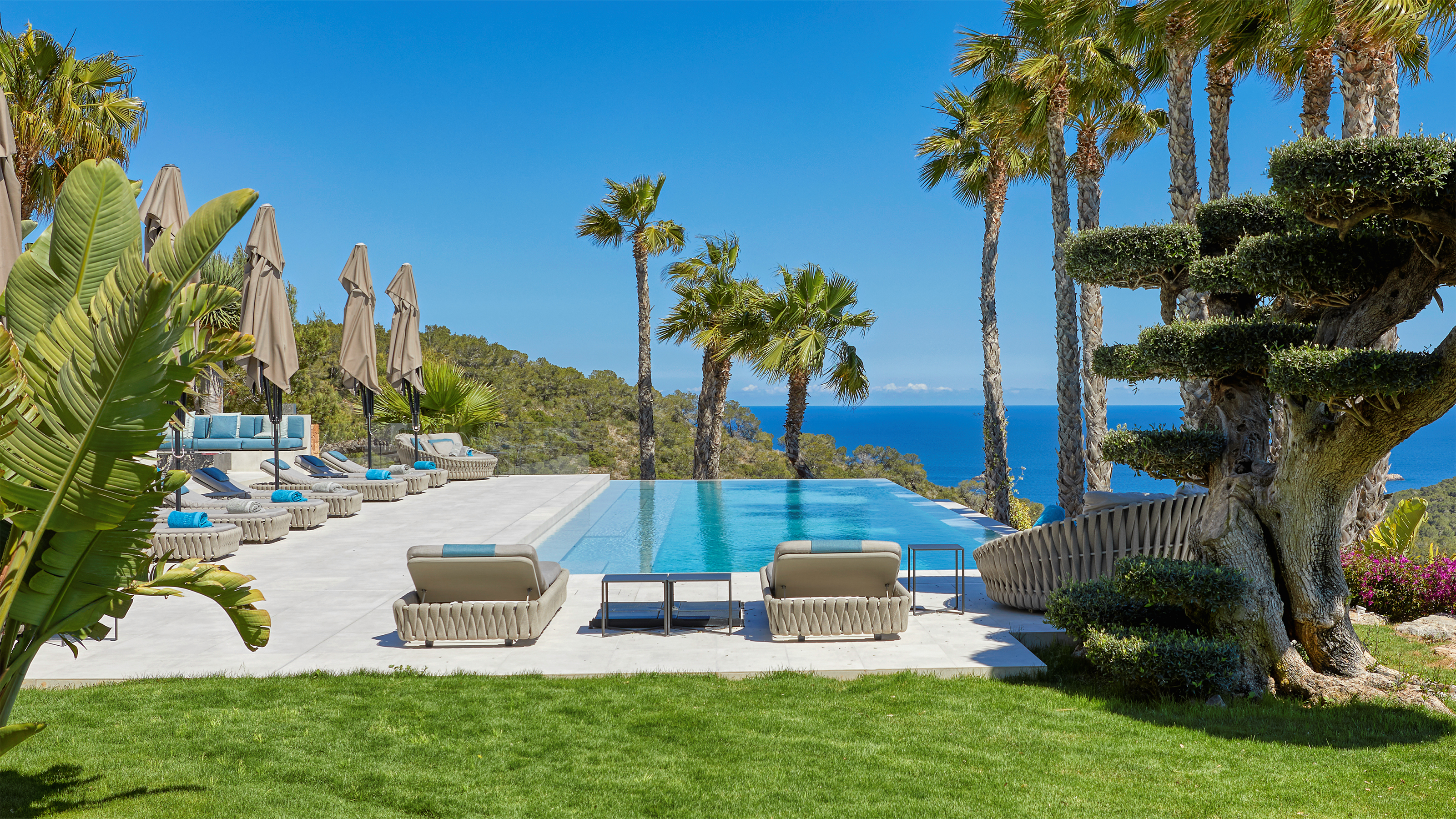 Dalles extérieures claires près d'une piscine à débordement avec vue mer et palmiers.