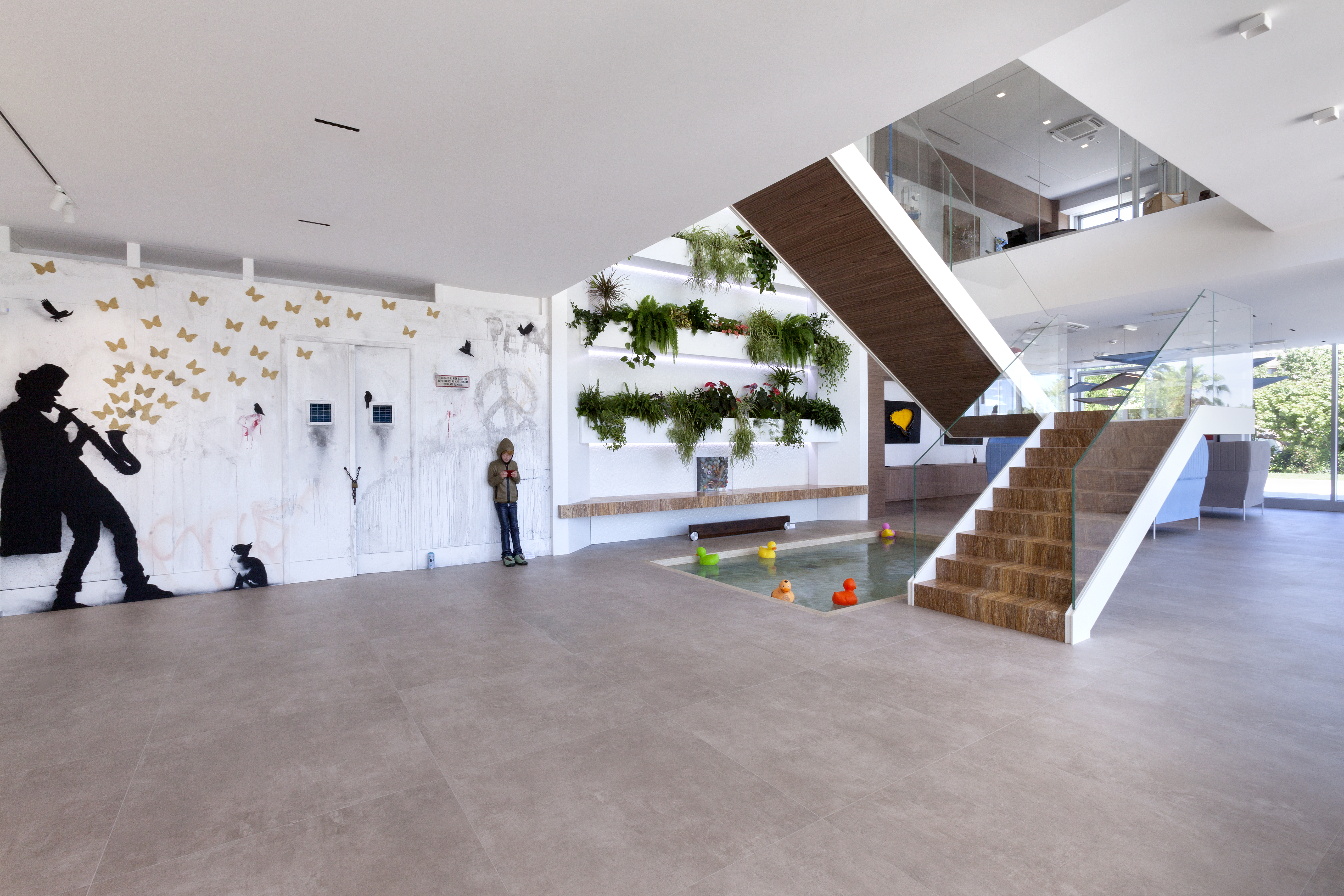 Showroom moderne avec carrelage clair, escalier élégant, mur végétal et art.