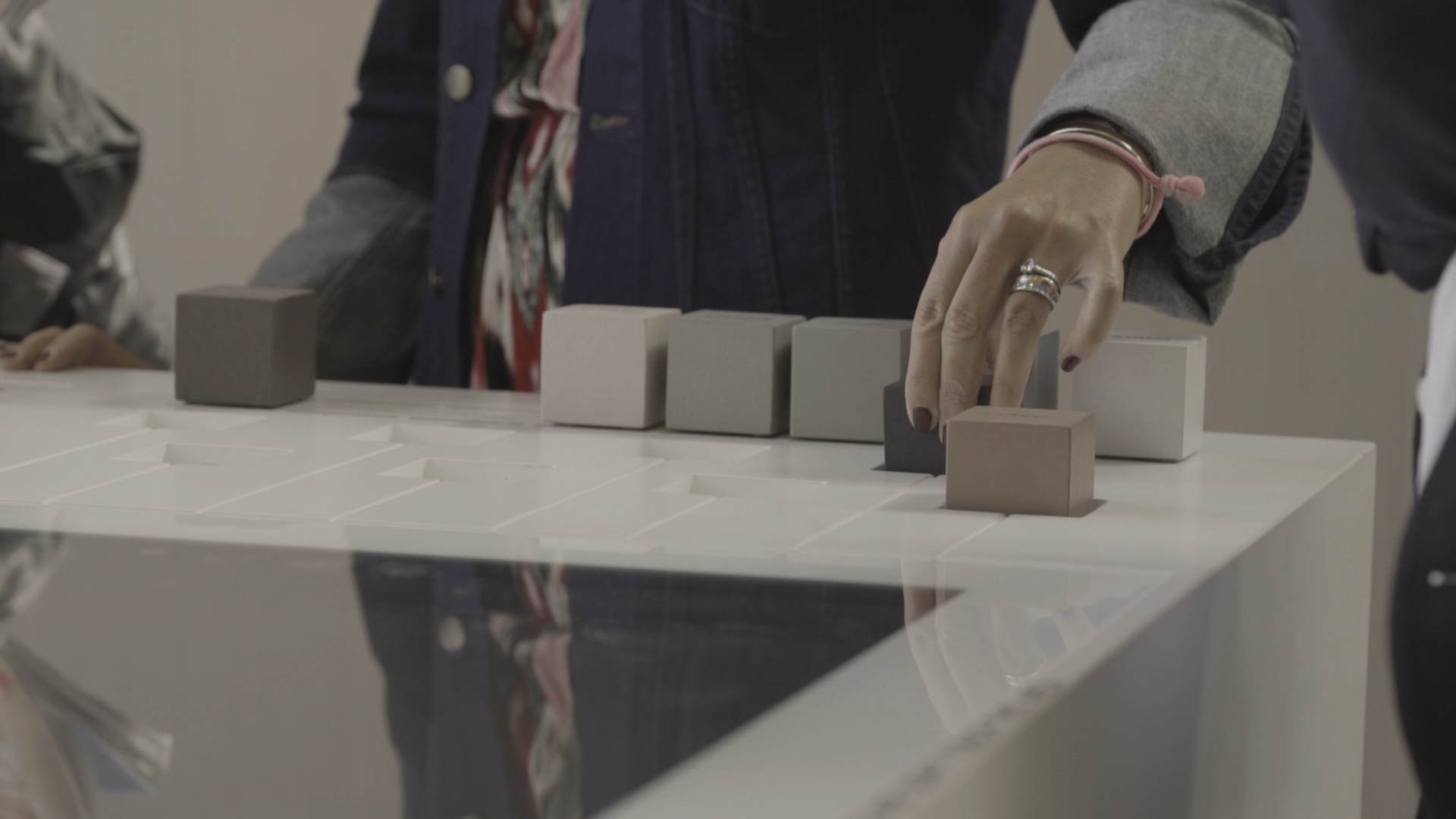 Une main choisit des motifs de carreaux dans différentes nuances de gris et de beige.