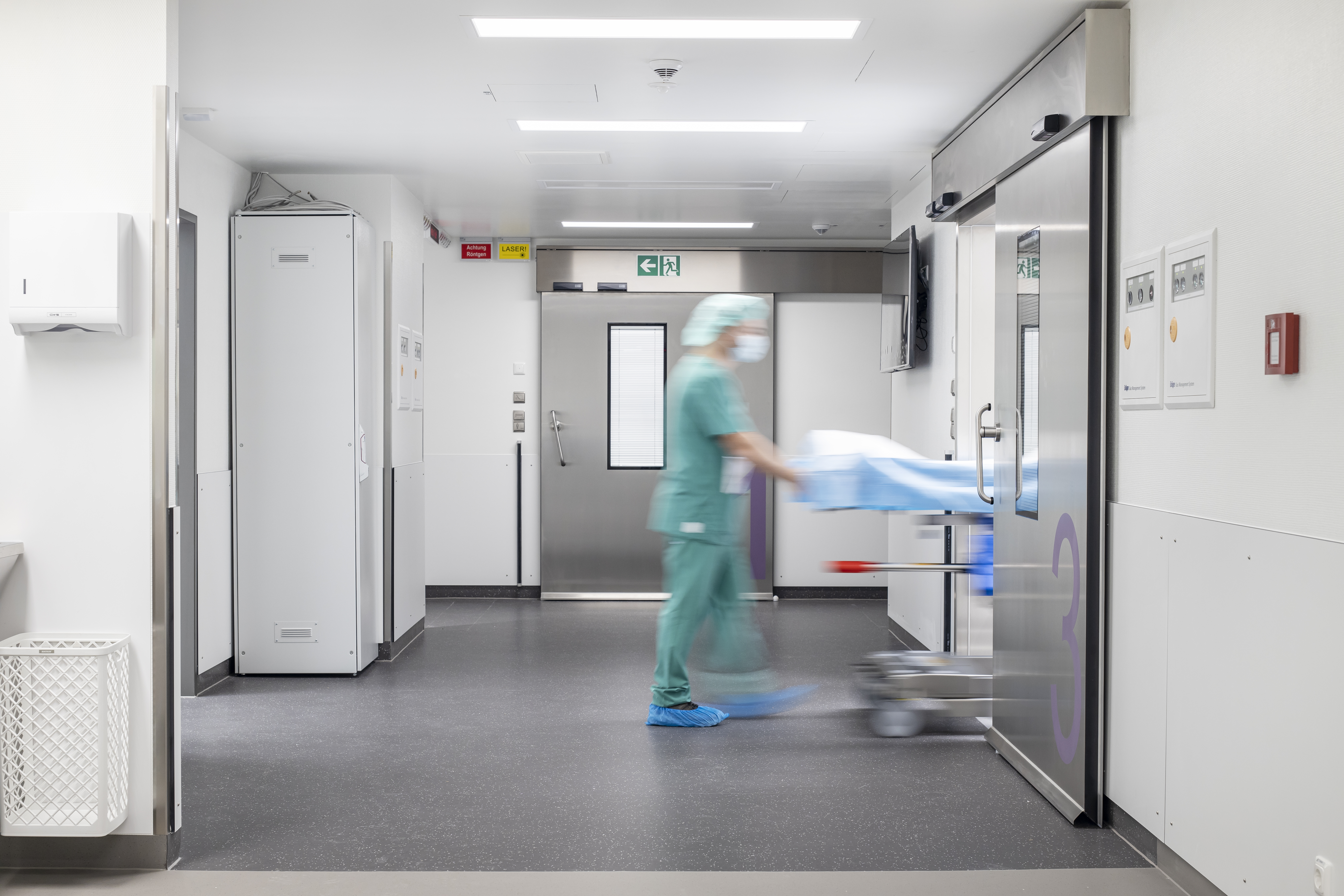 Couloir d'hôpital moderne avec carrelage sombre et personne en urgence avec civière.