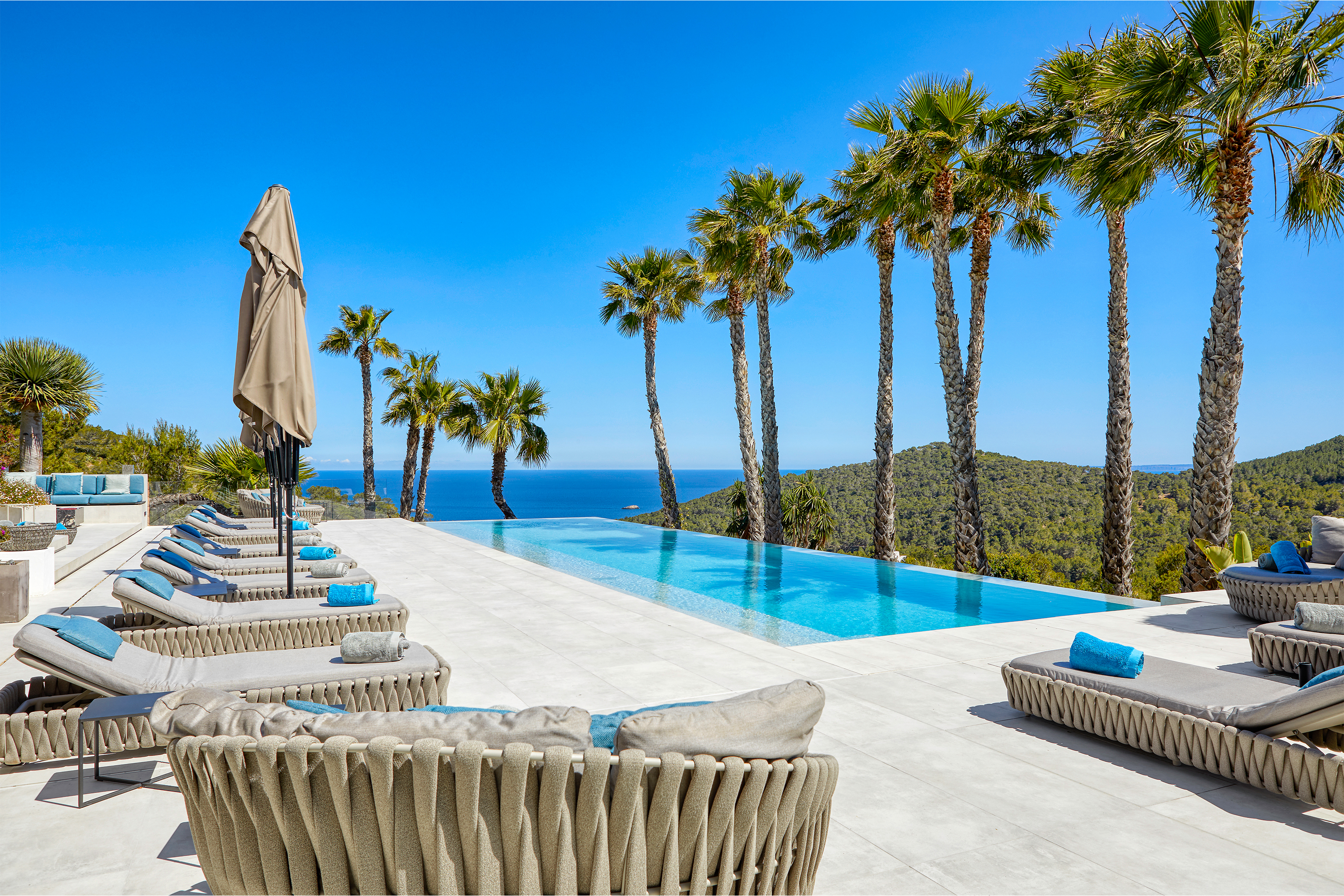 Zone de piscine luxueuse avec carrelage extérieur clair et vue sur mer sous les palmiers.